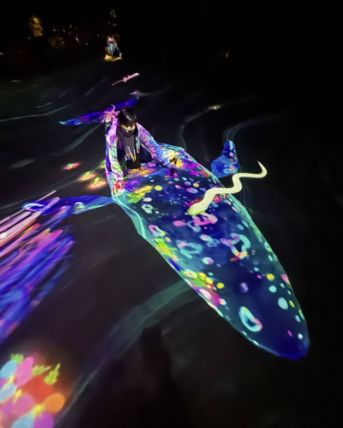 Man crouching over a glowing digital whale projection on the floor at teamLab Forest Fukuoka in Japan.