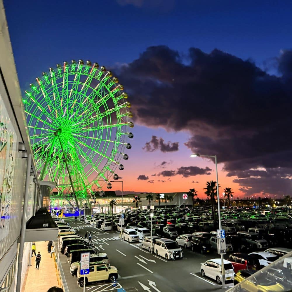 Illuminated green "Rinku no Hoshi" Ferris wheel against a sunset sky over the parking area at Rinku Premium Outlets in Osaka, Japan.