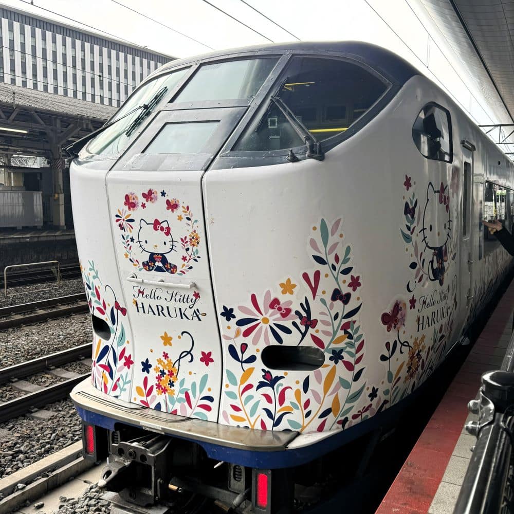 Sleek Hello Kitty Haruka limited express train with floral and character liveries stopped at a train station platform in Japan.