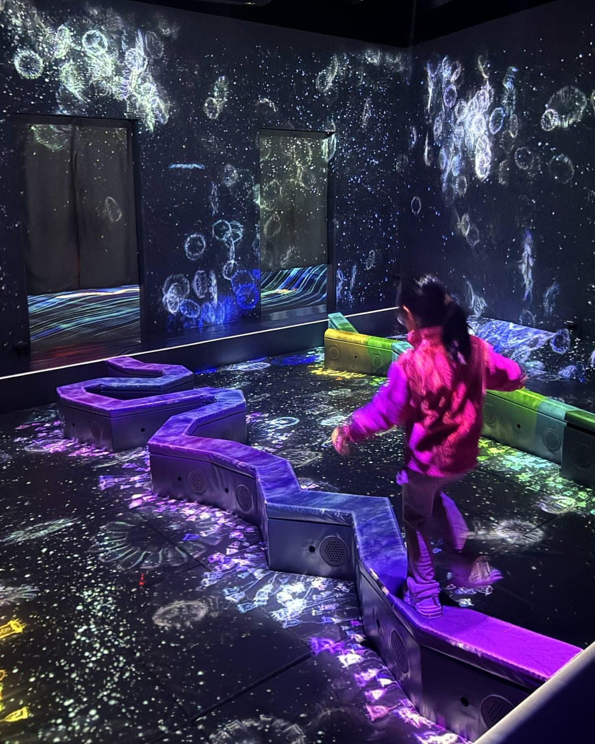 Child balancing on a zig-zag stepping path inside an interactive digital light exhibit at teamLab Forest Fukuoka in Japan.