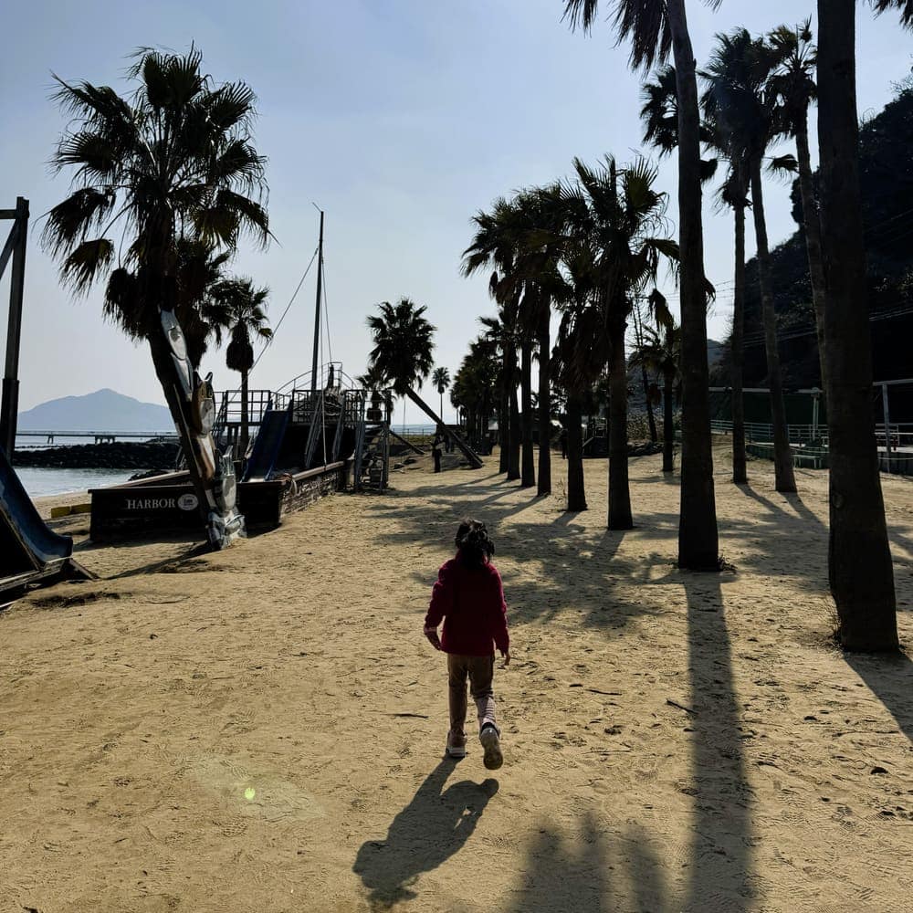 Palm-tree-lined sandy walkway and wooden ship playground along the coast of Itoshima in Fukuoka Prefecture, Japan.