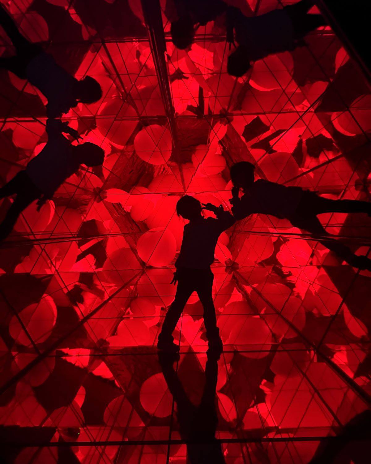 Child posing inside a red mirrored kaleidoscope light installation at teamLab Forest Fukuoka in Japan.