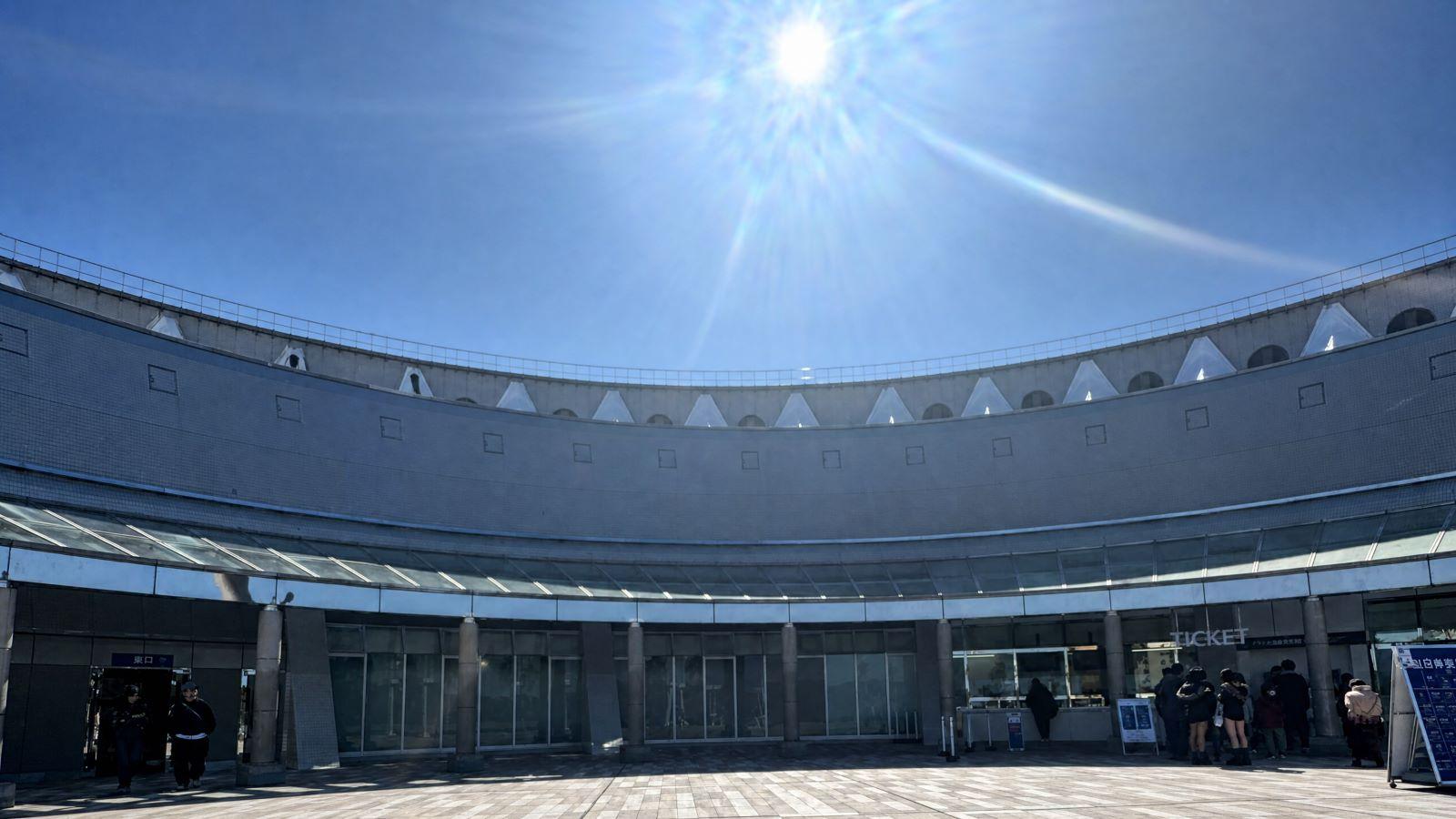Curved modern building exterior and sunlit entrance plaza at Marine World Uminonakamichi in Fukuoka, Japan.