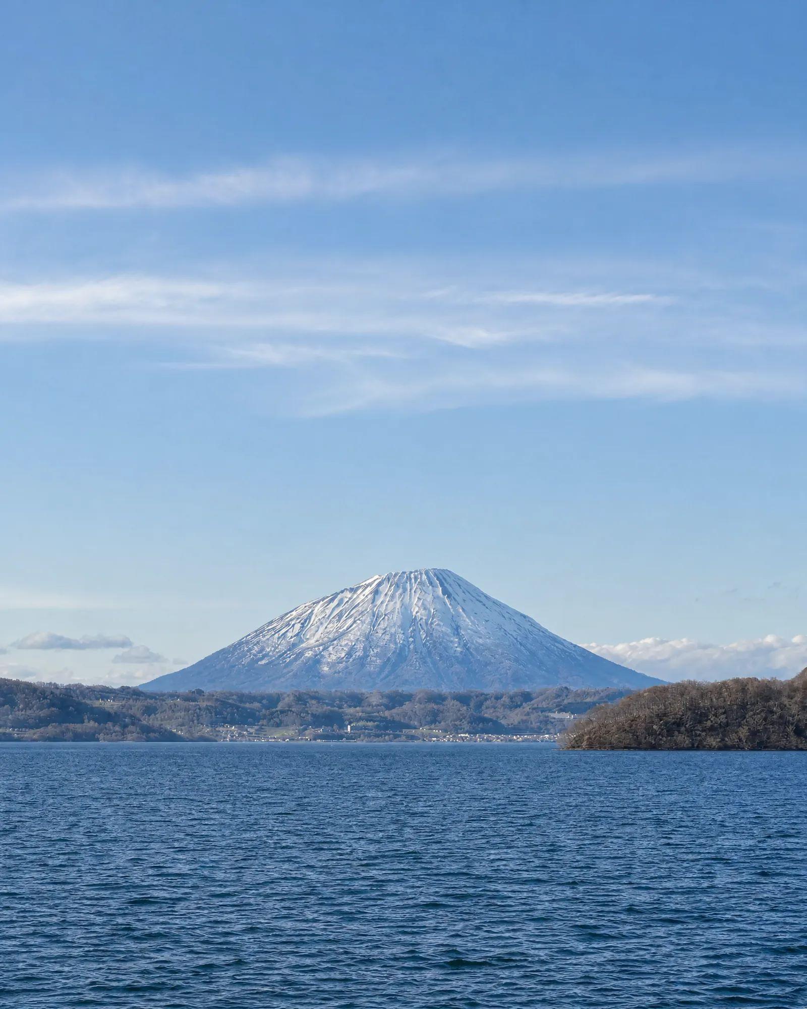 日本北海道洞爺湖蔚藍湖面後方,白雪覆頂的羊蹄山在晴空下聳立。